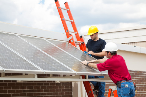 vue de 2 hommes dans une échelle en train d'installer un panneau solaire sur un toit