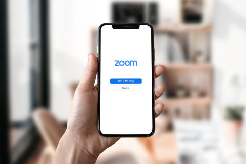 Vue du main tenant un téléphone sur lequel on voit l'application Zoom