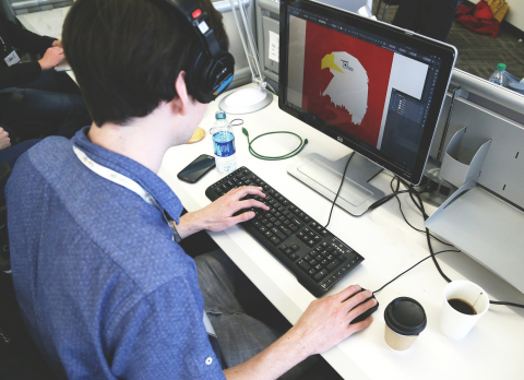 Vue d'un jeune homme devant son ordinateur en train de créer un logo représentant un aigle