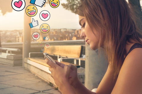 vue d'une femme regardant sont téléphone duquel émerge des logo de pouce en l'air, d'emoji et de coeur
