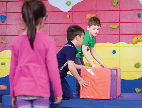 Vue de trois enfants jouant avec des blocs de mousse devant un mur d'escalade